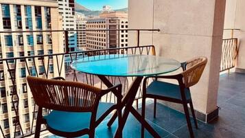 Un balcón con mesa y sillas de vidrio, con vista a un paisaje urbano de edificios altos.