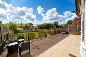Eine Terrasse mit Gartenmöbeln, einem Grillbereich und Blick auf einen Garten und den Himmel.