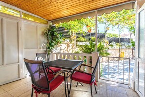 A covered patio with a table and chairs, a view of the garden, and a white door. - A1 - Cozy apt w Pool & big Terrace, 2 min to Beach (Dugi Rat)