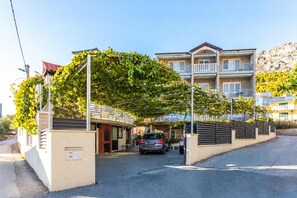 A multi-story residential building with a covered parking area and a car parked in front. - A1 - Cozy apt w Pool & big Terrace, 2 min to Beach (Dugi Rat)