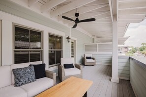 Un porche techado con ventilador de techo, muebles de mimbre y vistas al vecindario.