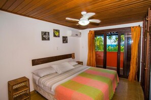 A bedroom with a bed, a ceiling fan, a window with curtains, and a view of greenery outside. - Casa Giada - Oceanfront Villa in Praia do Forte - Private Pool and 4 Suites (Acu da Torre (Praia do Forte))