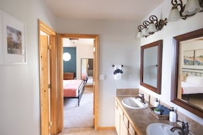 Ein Schlafzimmer mit Bett, ein Badezimmer mit Waschbecken und Spiegel sowie ein Flur zu einem weiteren Raum.