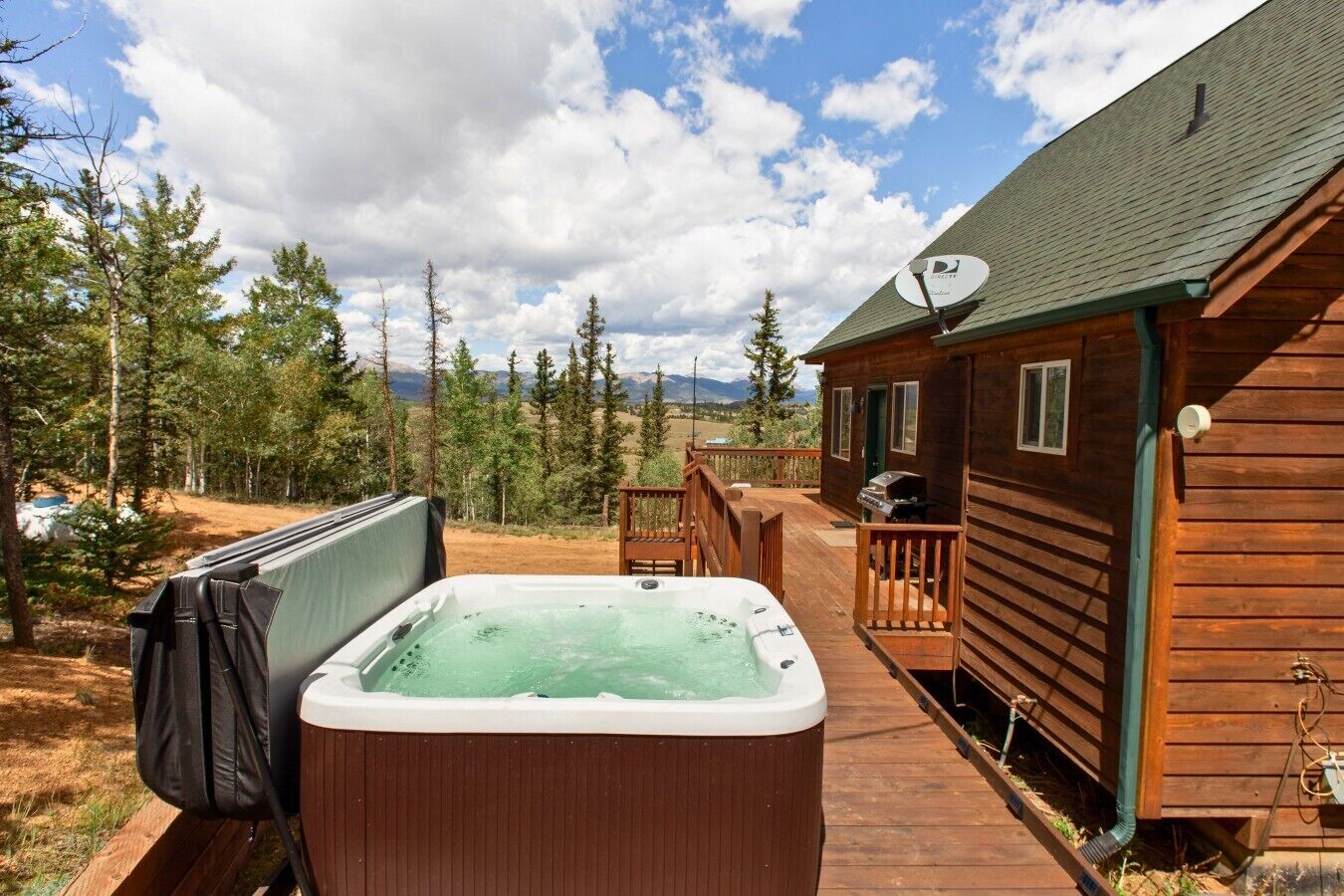 En stuga av trä med ett bubbelbad, en veranda och en satellantenn.