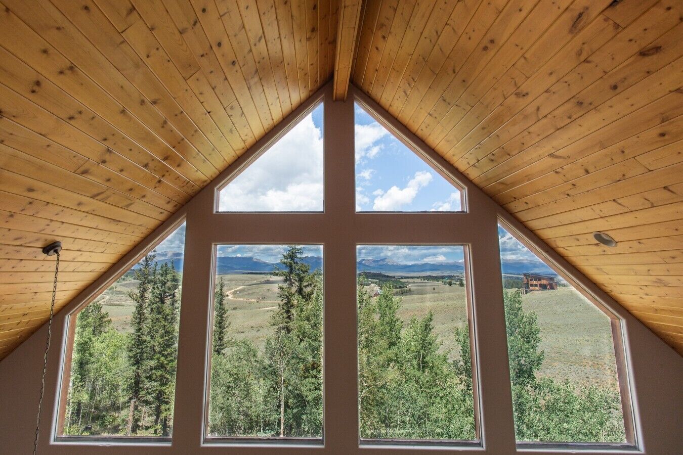 Ein Zimmer mit schräg verlaufender Holzbalkendecke und großen Fenstern mit Blick auf eine Berglandschaft.