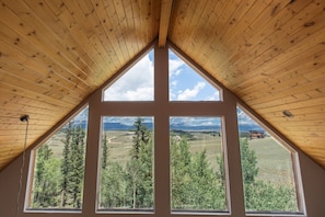 Una habitación con techo de madera inclinado y ventanas amplias que ofrecen vistas a un paisaje montañoso.