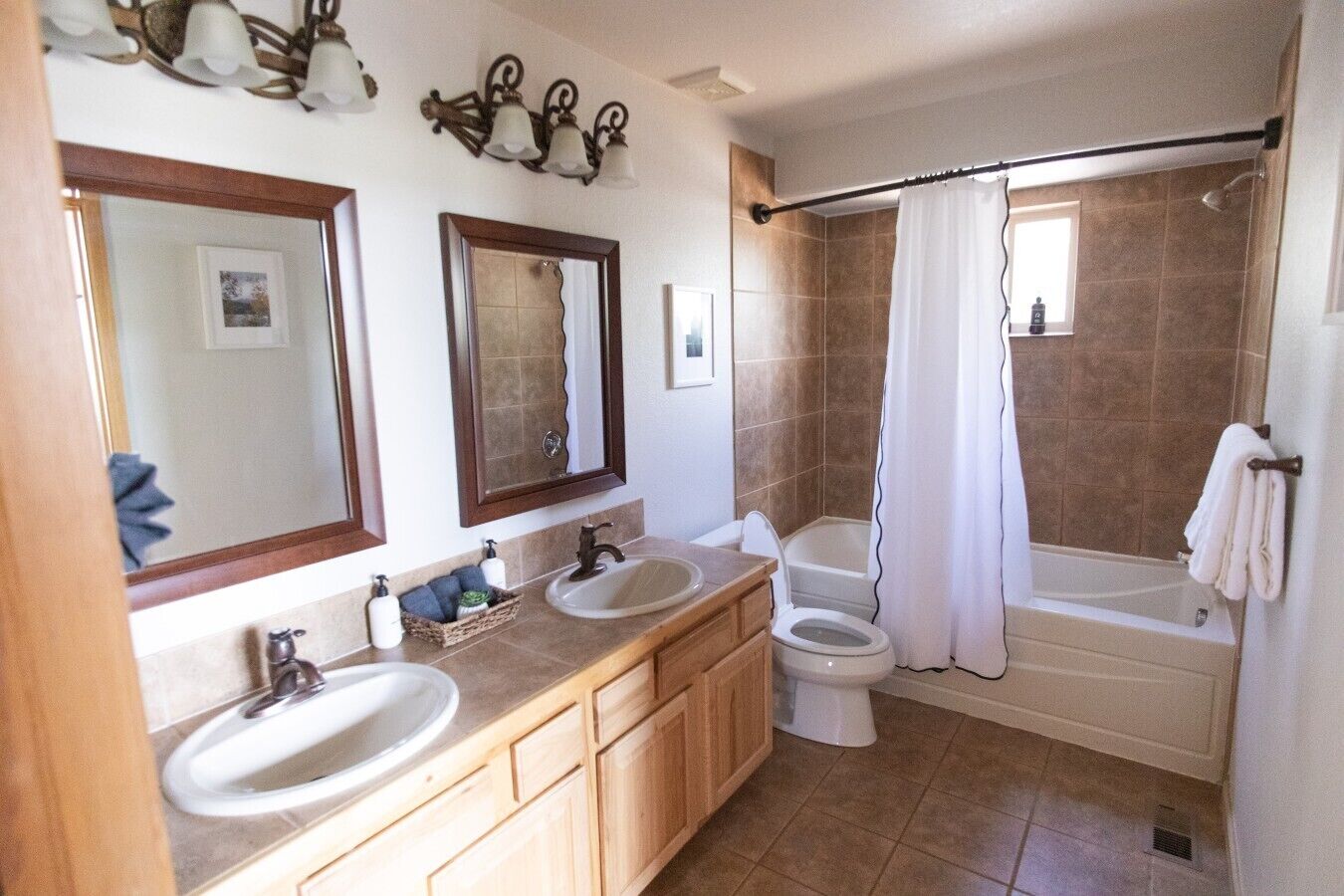 Ein Badezimmer mit einem Doppelwaschbecken, Toilette und Badewanne. Über den Waschbecken befinden sich Spiegel und ein Duschvorhang ist zu sehen.