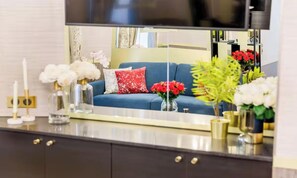 Un salon moderne avec un canapé bleu, des coussins décoratifs et des compositions florales disposées sur une surface réfléchissante.