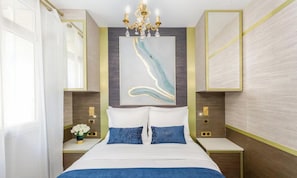 Habitación de hotel con una cama grande, un candelabro, una obra de arte en la pared, mesitas de noche y un espejo.
