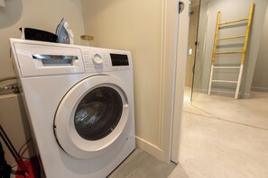 A front-loading washing machine in a laundry room with a wooden ladder and a door leading to another room. - Vacation rental in Haute-Loire with a pool and views of the countryside—perfect for relaxing (Paulhaguet)