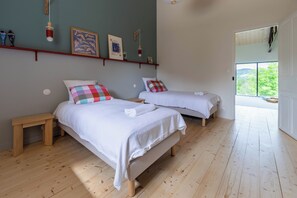 A bedroom with two beds, wooden flooring, and a view through an open door. - Vacation rental in Haute-Loire with a pool and views of the countryside—perfect for relaxing (Paulhaguet)