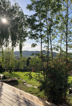 A wooden deck with a stone pathway leading to a lush garden with various trees and shrubs. - Vacation rental in Haute-Loire with a pool and views of the countryside—perfect for relaxing (Paulhaguet)