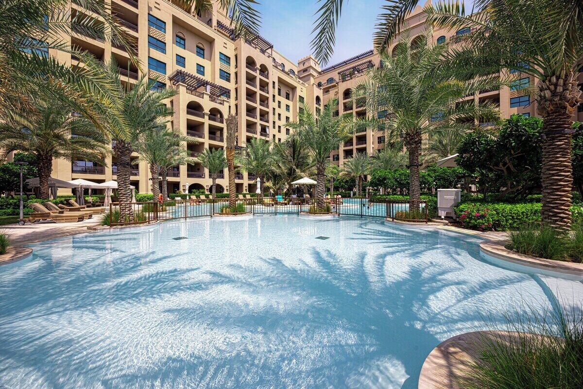 Ein Hotel mit großem Pool, umgeben von Palmen und Liegestühlen.