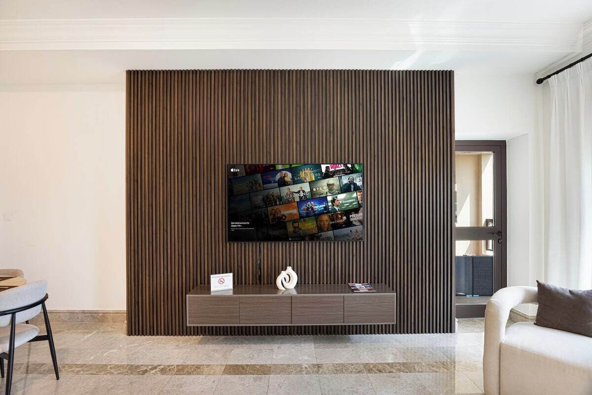 A modern living room with a flat-screen TV mounted on a wooden panel wall, a marble floor, and a sofa.