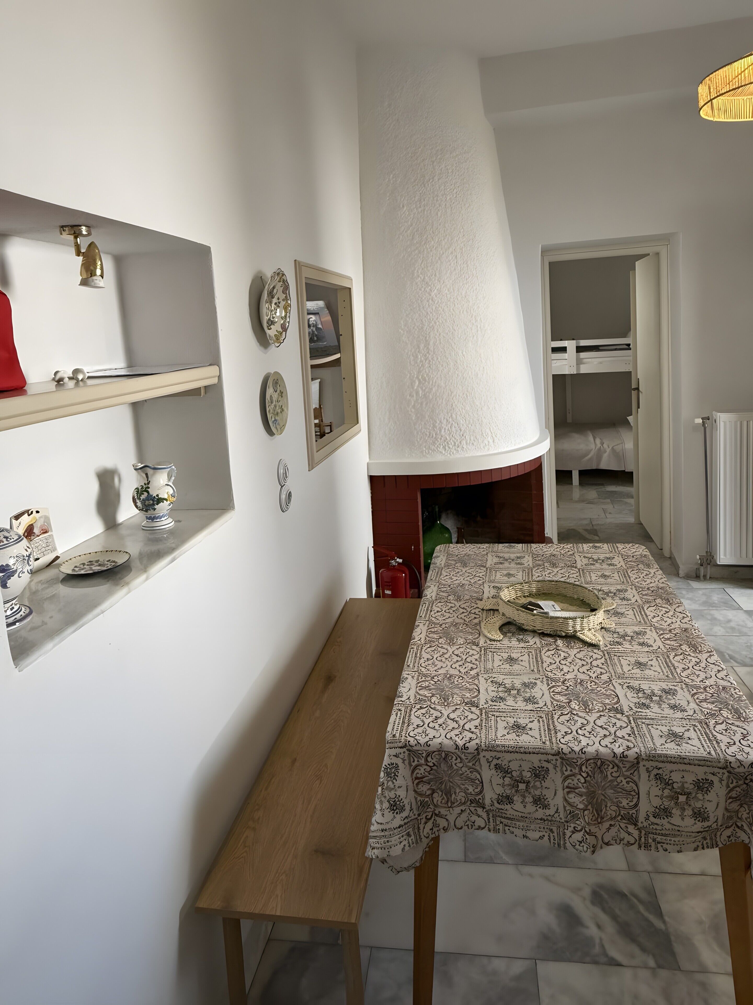 A dining area with a table covered by a patterned tablecloth, a wooden bench, and a wall-mounted shelf with decorative plates.