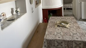 A dining area with a table covered by a patterned tablecloth, a wooden bench, and a wall-mounted shelf with decorative plates. - SimpleGreece Skyros Traditional Holiday Home with Balcony, Wi-Fi & Air Conditioning (Σκύρος)