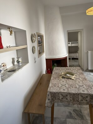 Zona pranzo con tavolo ricoperto da una tovaglia fantasia, una panca in legno e una mensola a parete con piatti decorativi.