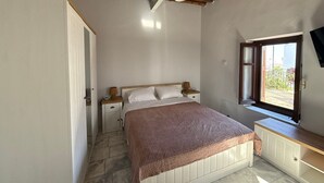 A bedroom with a wooden ceiling, a bed with white bedding, a nightstand, a bedside lamp, and a window with a view. - SimpleGreece Skyros Traditional Holiday Home with Balcony, Wi-Fi & Air Conditioning (Σκύρος)
