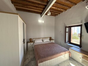 Una camera da letto con soffitto in legno, un letto con biancheria bianca, un comodino, una lampada da letto e una finestra con vista.