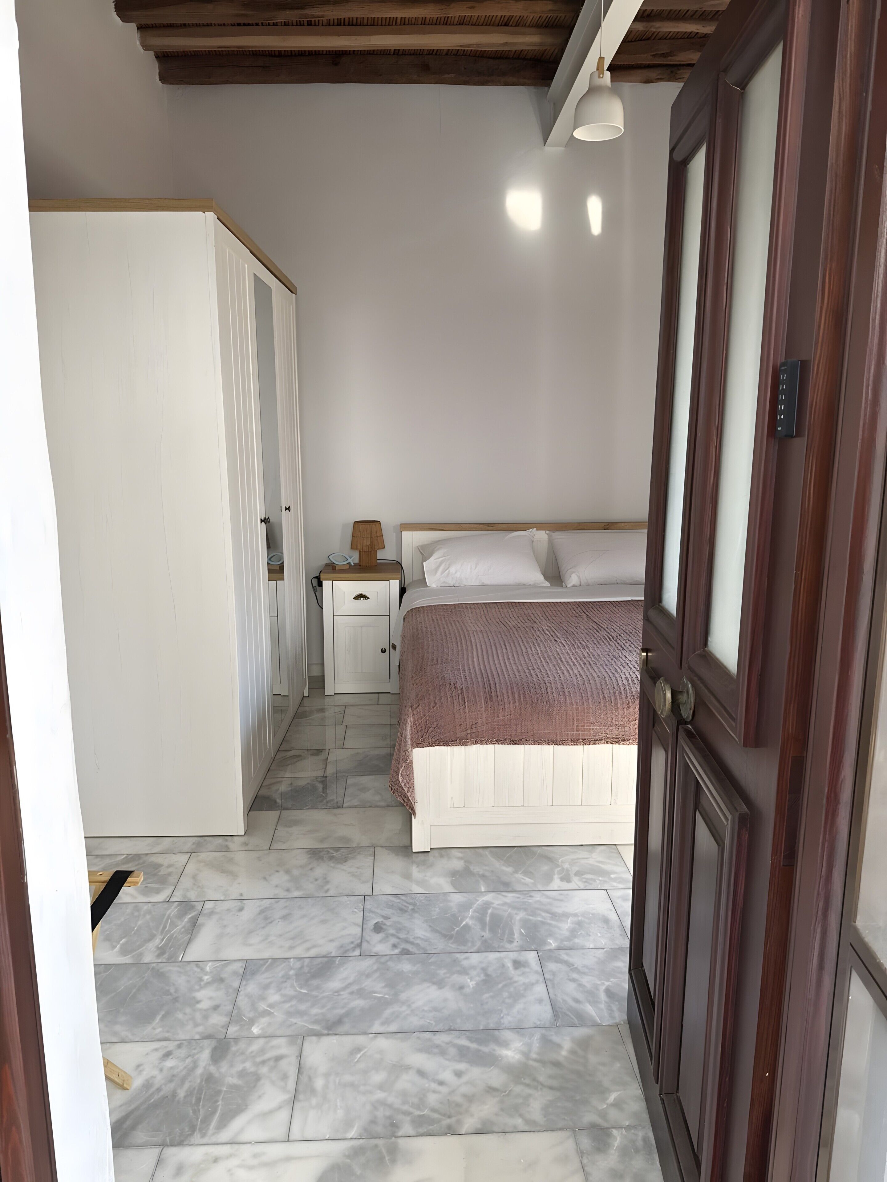 A bedroom with a bed, bedside table, lamp, wardrobe, and a door.