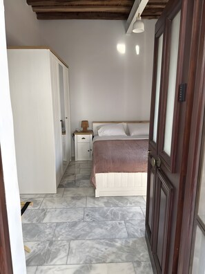 A bedroom with a bed, bedside table, lamp, wardrobe, and a door.