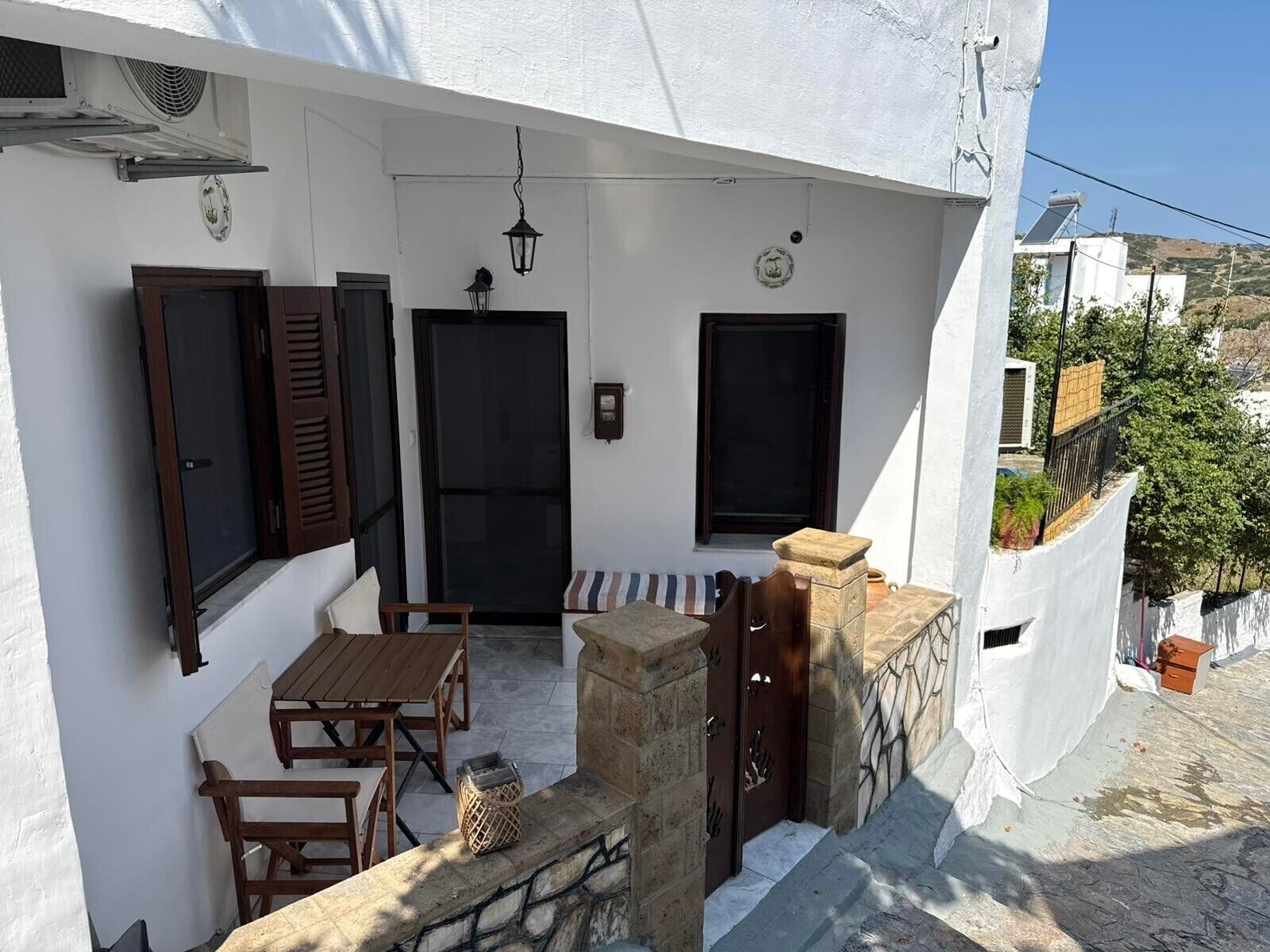 A white building with a balcony, wooden furniture, and a stone bench.