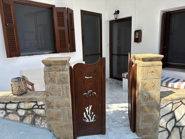 A stone entrance with a wooden door featuring a leaf design, a wicker basket, and a chair.
