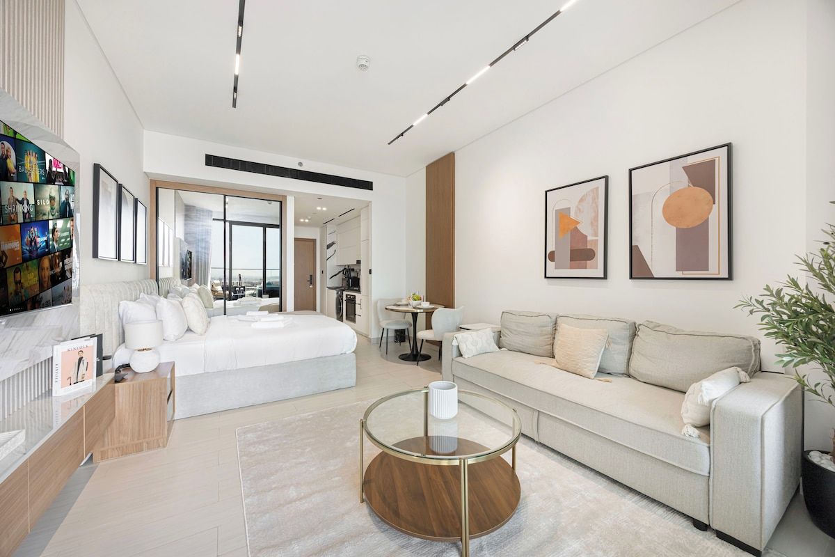 Quarto de hotel moderno com cama, sofá, mesa de centro de vidro e obras de arte nas paredes.