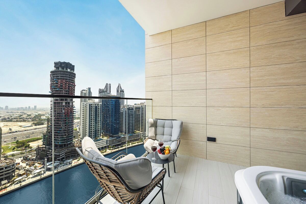 Un balcon avec vue sur les toits de la ville, un jacuzzi et deux fauteuils avec un panier de fruits.
