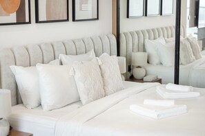A neatly made bed with white linens and pillows, a bedside lamp, and a mirror reflecting the room. - Private Jacuzzi / Canal Views / Pool & Gym (Dubai)