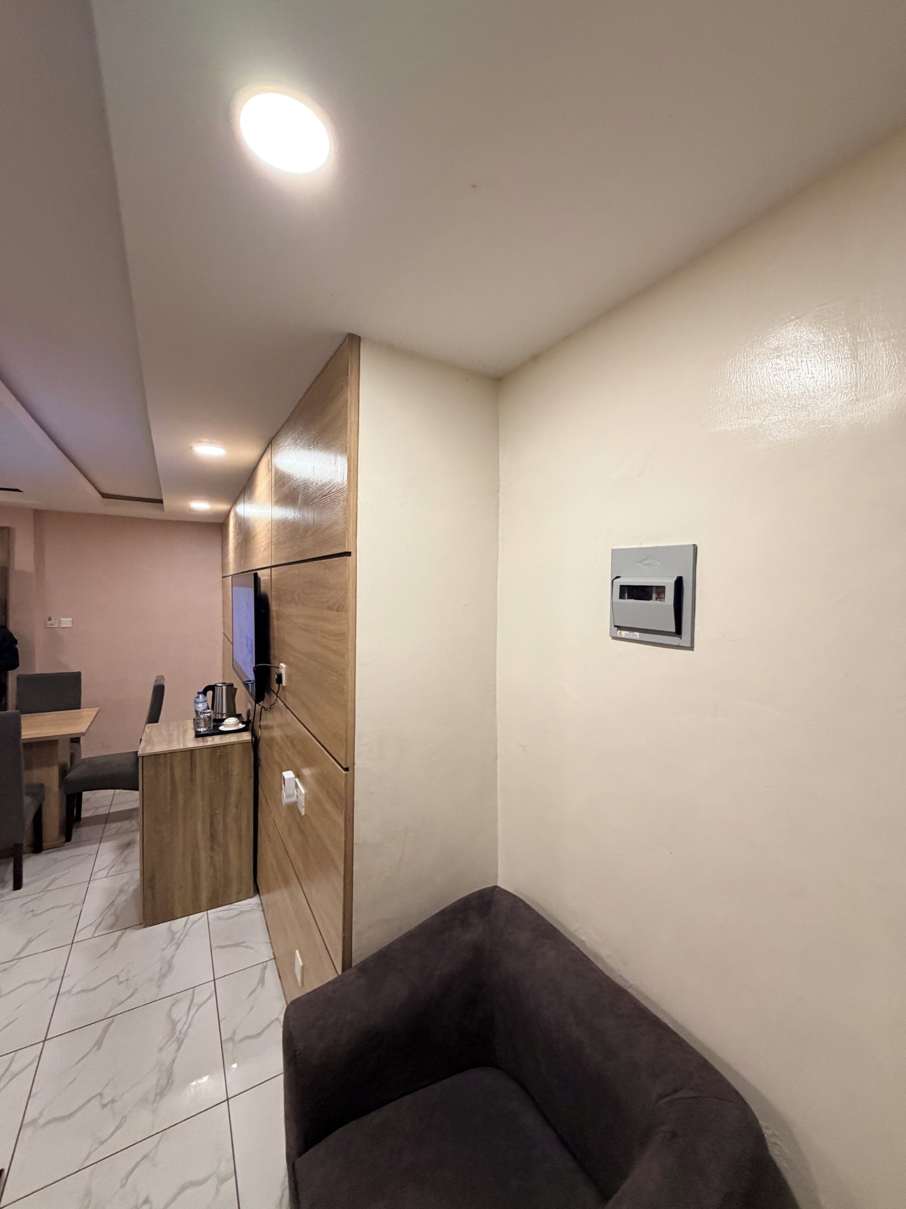 Habitación de hotel con zona de estar, una mesita con tetera, televisión y un dispositivo en la pared.