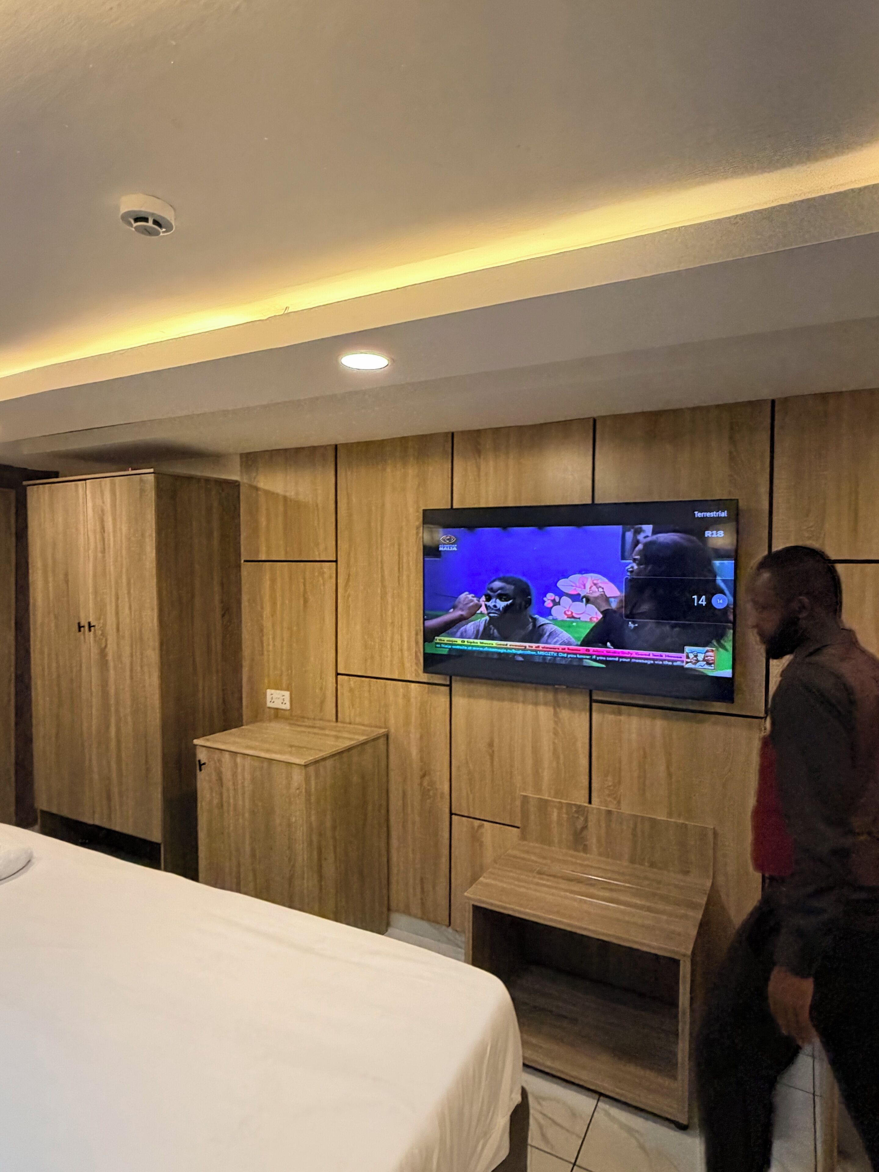 A hotel room with a bed, a television mounted on the wall, and wooden paneling.