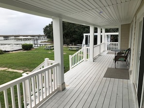 A covered outdoor deck with white railings, picnic tables, and a view of a water body and bridge. - Water Front Delight - Private Beach and Dock, Wi-fi, Pet Friendly, 3 Master BR's (Norfolk)