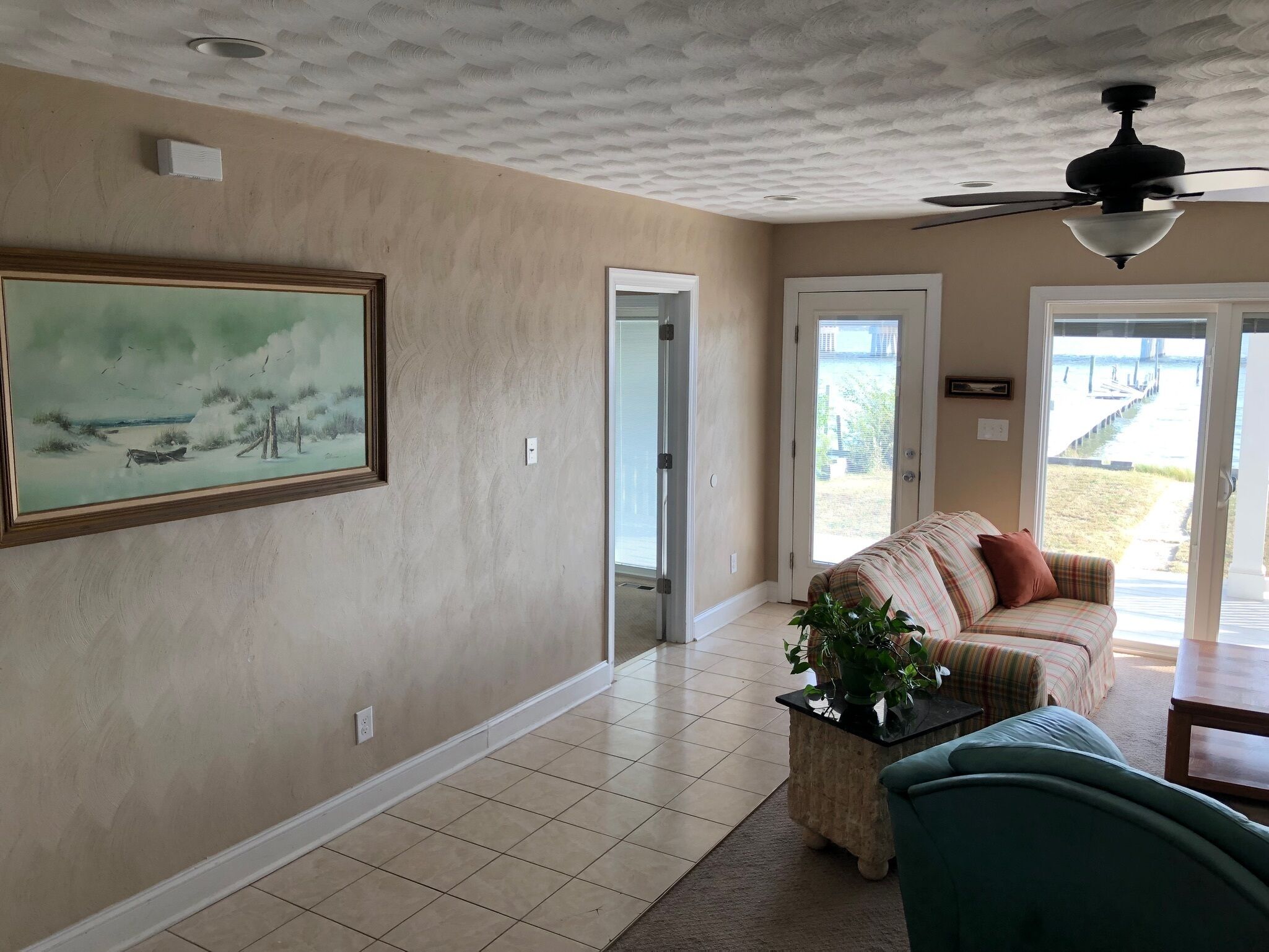 A living room with a beige wall, a framed painting, a sofa, a coffee table, and a ceiling fan.