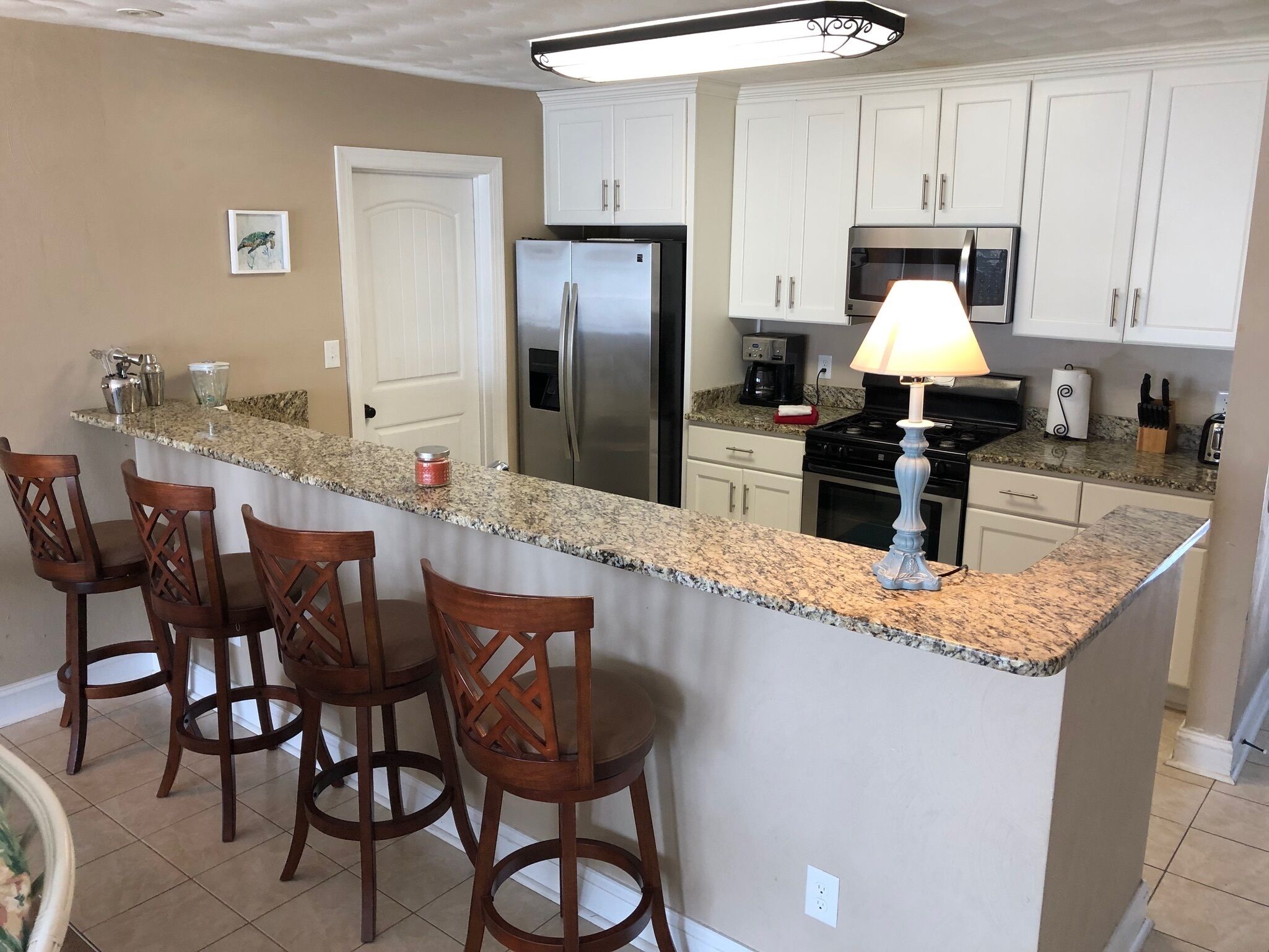 A kitchen with a central island, bar stools, a refrigerator, a stove, and a microwave.