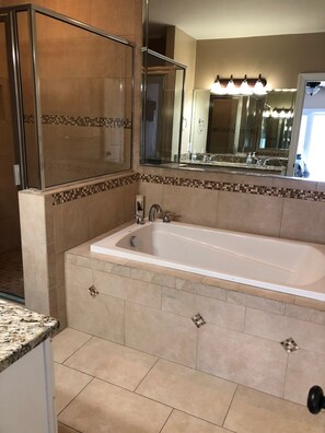 Een badkamer met een groot bad, een douche en een wastafel met spiegel.