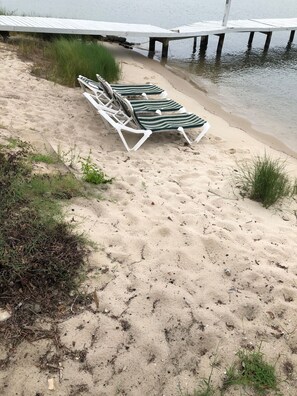 Een zanderig strand met ligbedden en een houten pier die in het water uitloopt.