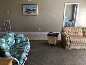 A living room with a floral sofa, a plaid sofa, a small table, and a painting on the wall. - Water Front Delight - Private Beach and Dock, Wi-fi, Pet Friendly, 3 Master BR's (Norfolk)