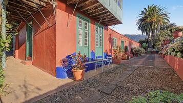 Una estrecha calle adoquinada con edificios pintados de rojo y azul, macetas con plantas y un cielo despejado.