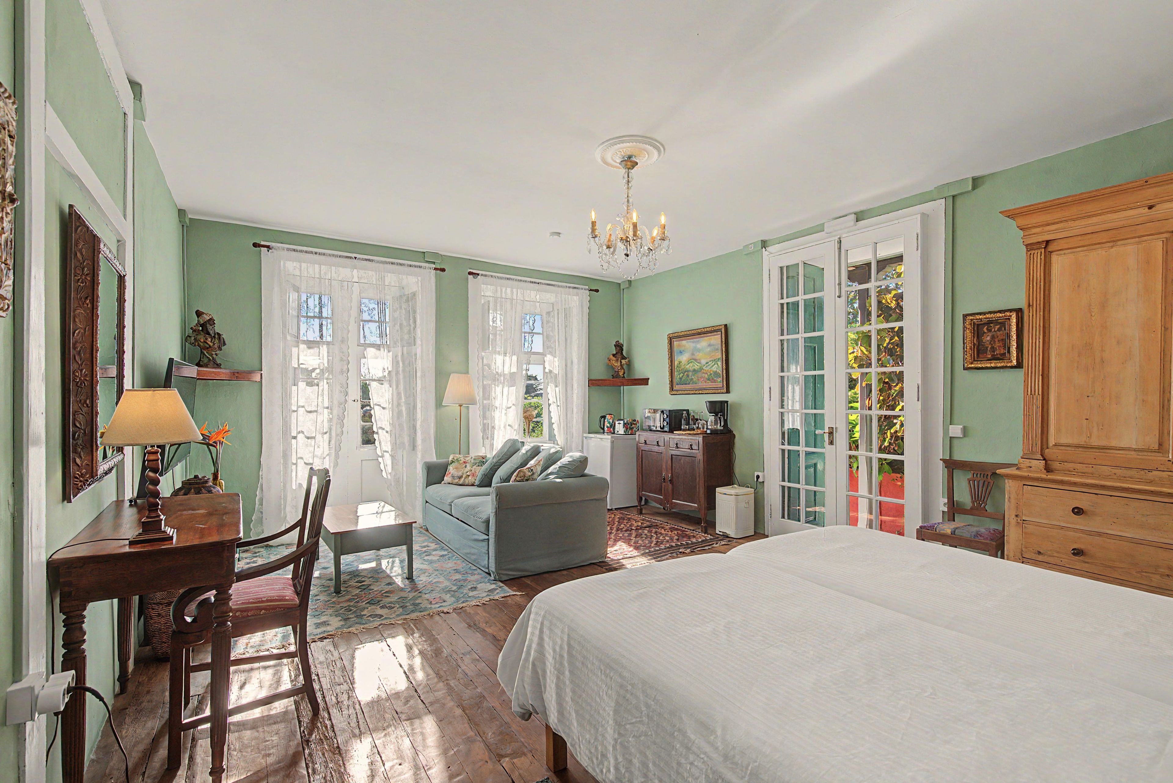 Ein Schlafzimmer mit Bett, Schreibtisch, Sessel, Sofa, Kommode und einer Chandelier.
