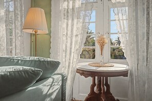 Una habitación con un sofá, una mesa con un florero y una ventana con cortinas de encaje.
