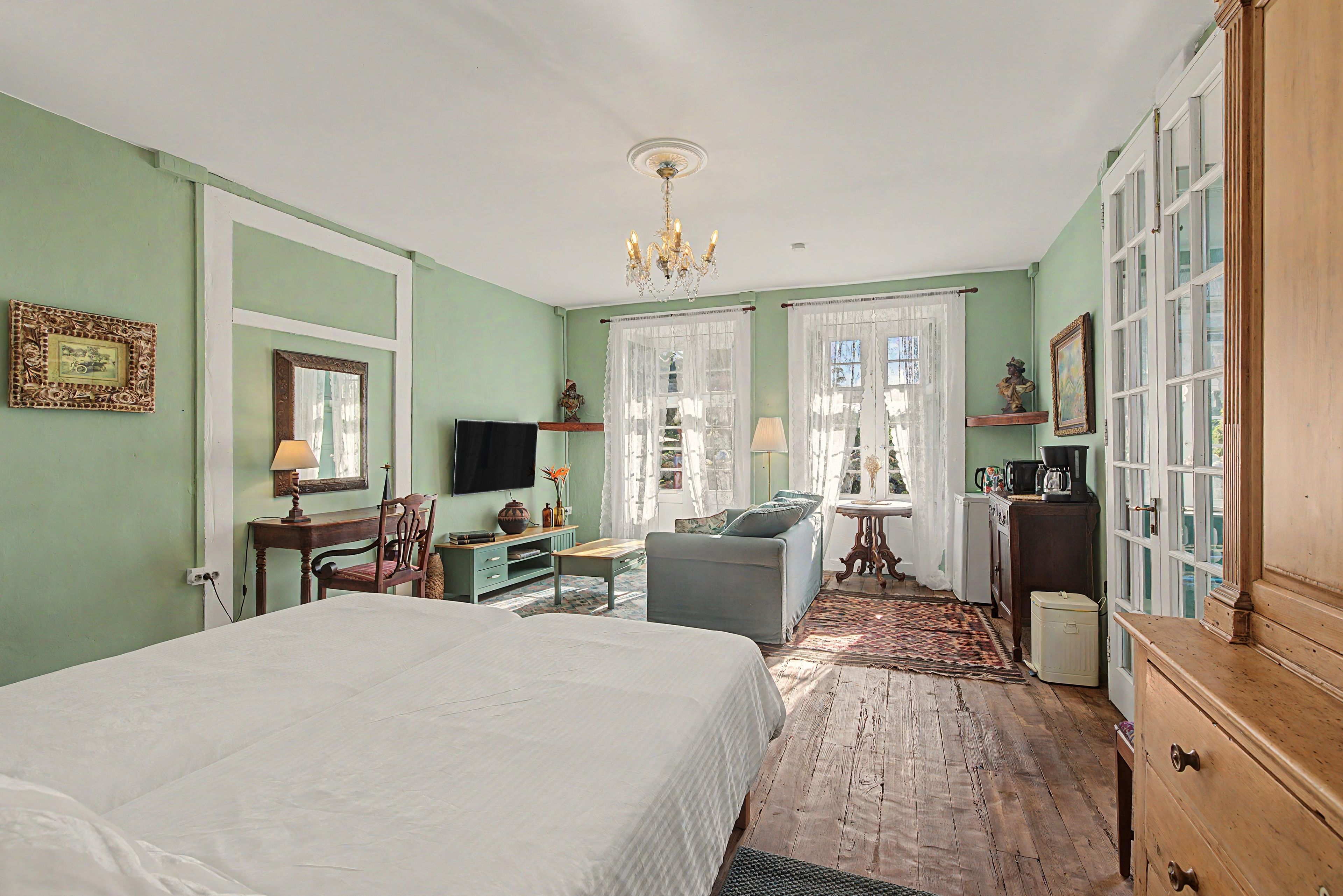 Quarto com cama, escrivaninha, cadeira, televisão, cômoda e janela com cortinas.