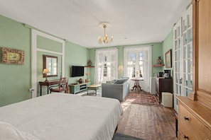 Une chambre à coucher comprenant un lit, un bureau, une chaise, une télévision, une commode et une fenêtre avec des rideaux.