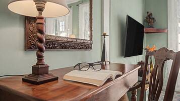 A wooden table with a lamp, a book, glasses, and a mirror.