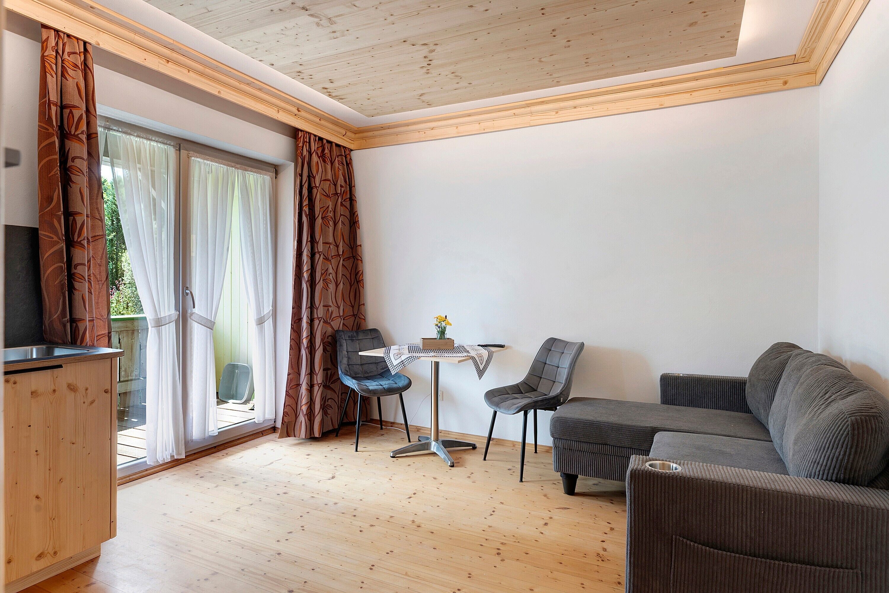 Ein modernes Wohnzimmer mit Holzboden, einer Couch, zwei Sesseln, einem kleinen Tisch und einem Fernseher.