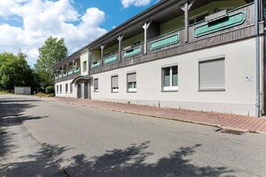 A two-story building with a balcony on the upper floor, a garage door on the ground floor, and a paved driveway.