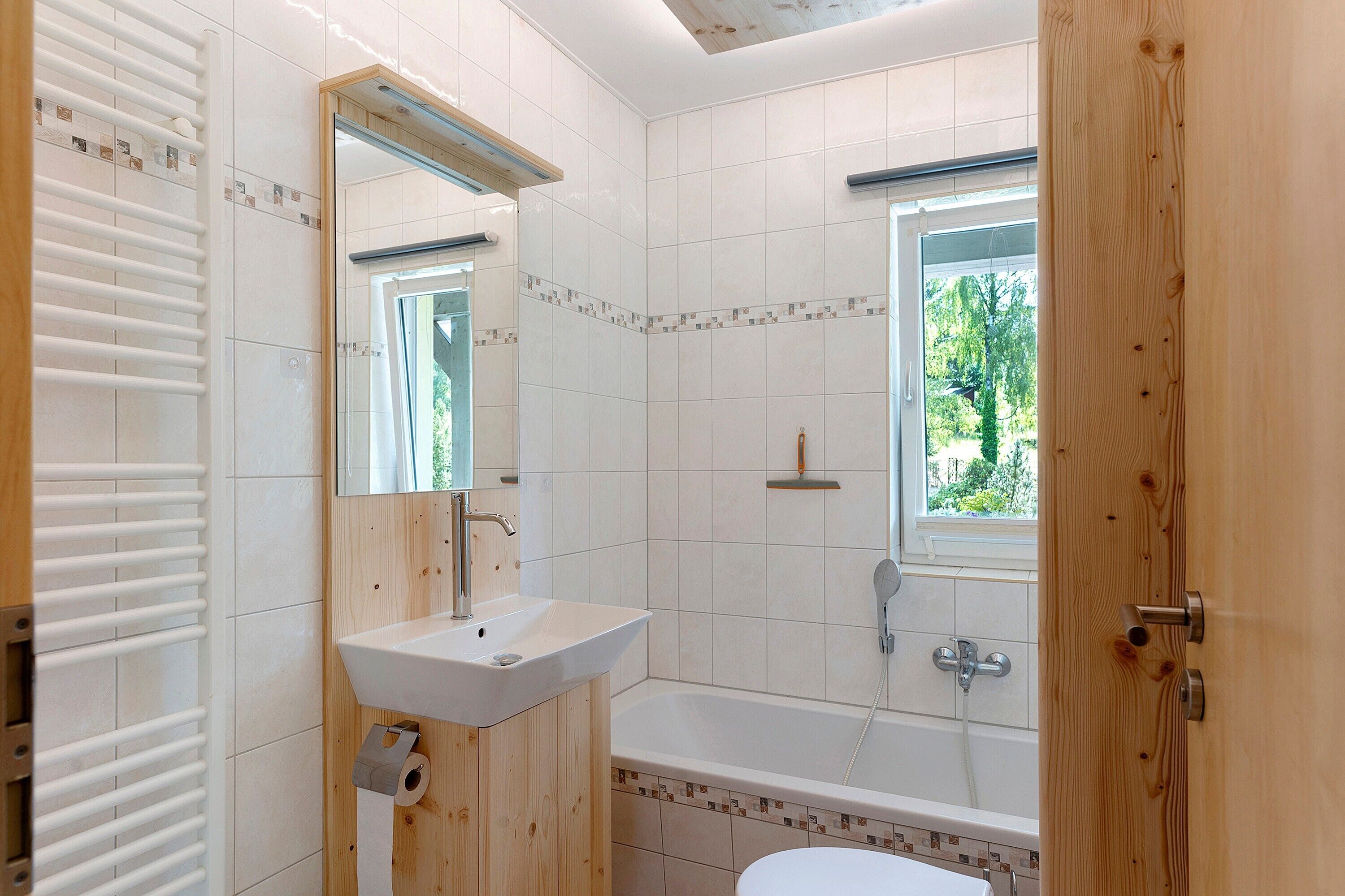 Ein Badezimmer mit einem weißen Waschbecken, einem Spiegel, einer Dusche und einem Fenster.