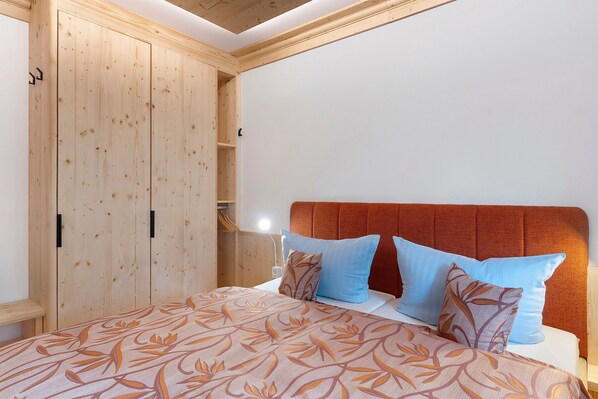 A bedroom with a wooden wardrobe, a bed with patterned bedding, and a red upholstered headboard.