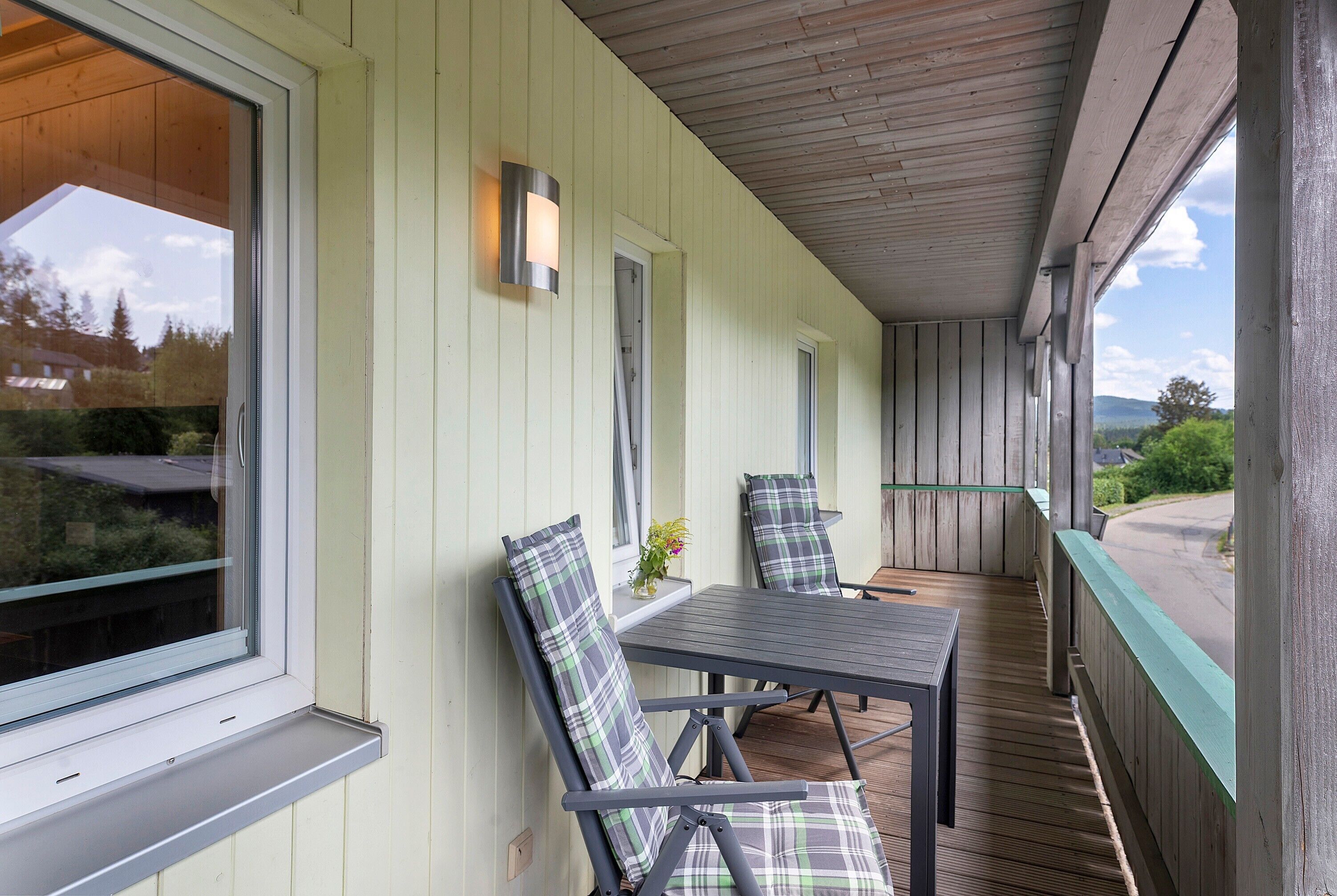 A covered porch with two chairs and a table, wooden walls, and a view of the landscape.