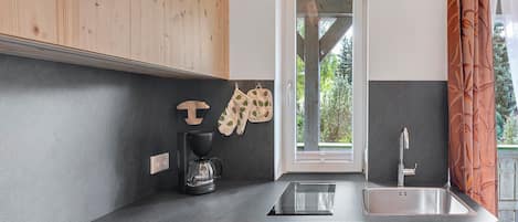 Una cocina moderna con encimera negra, armarios de madera, cafetera y pileta de acero inoxidable.